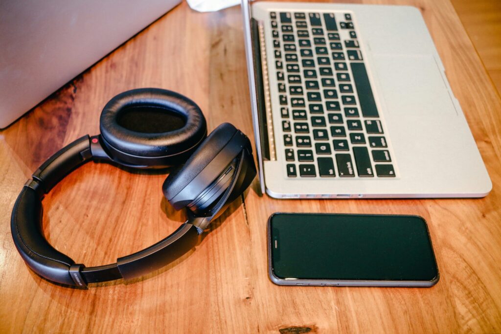 A laptop, iphone, and a pair of black headphones on a table