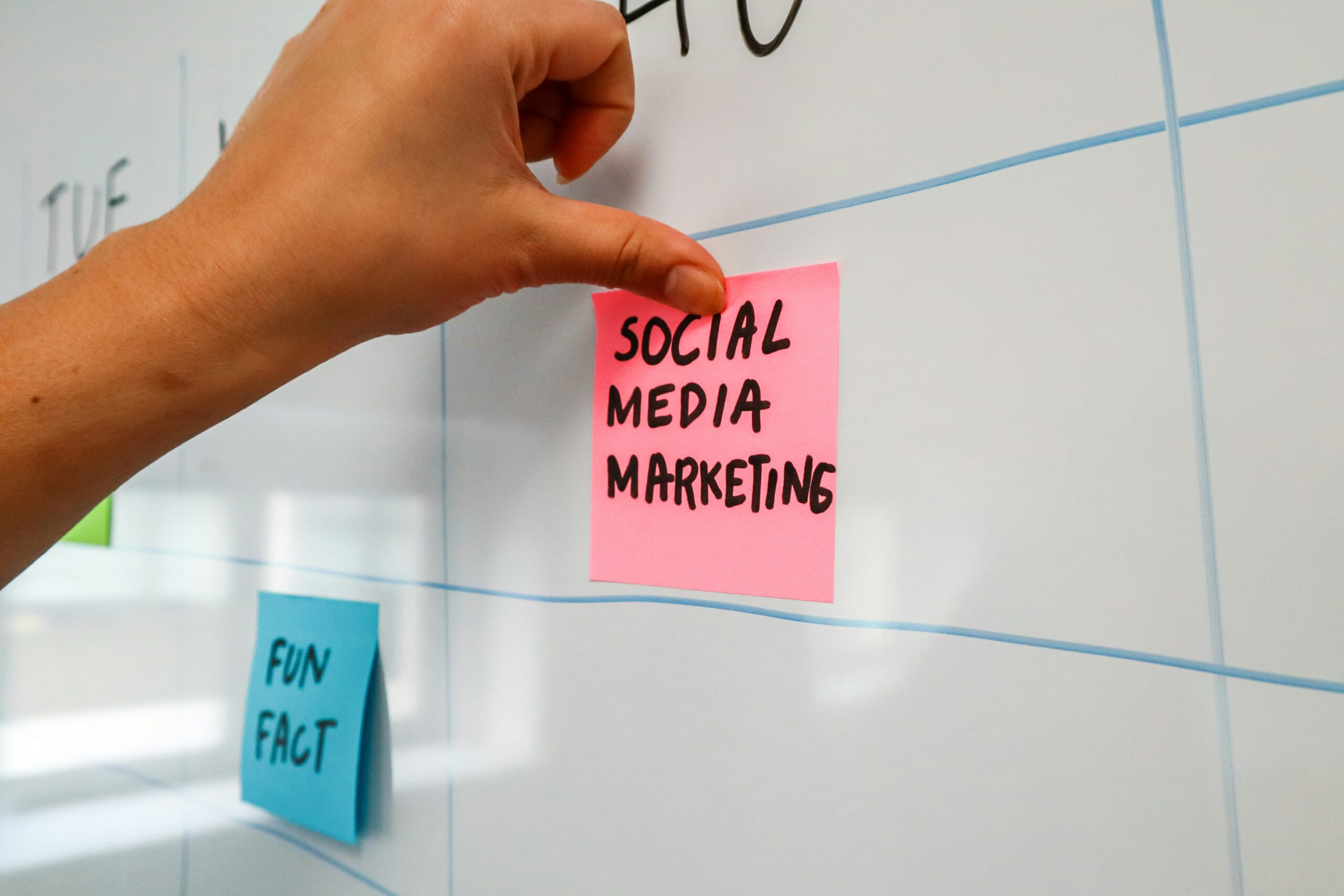Hand putting sticky note on a white board with the words media marketing on it