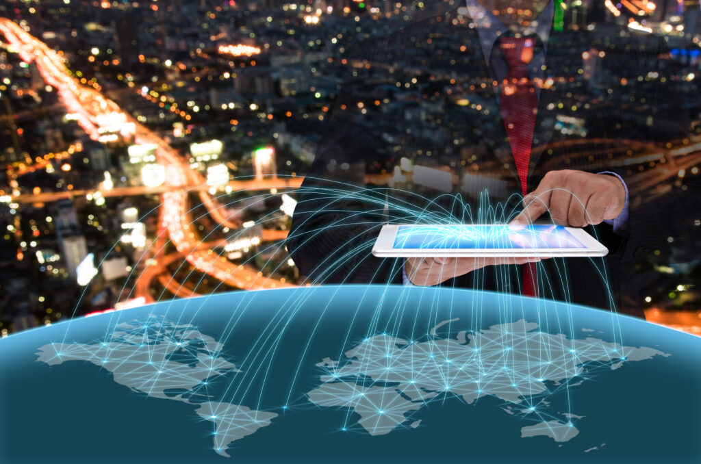 Business professional using a tablet to manage global digital networks, with a world map visualization and data connections over a city at night.
