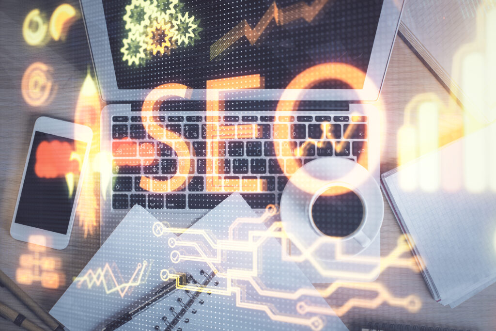 Laptop workspace with SEO text overlay, charts, gears, and digital data visuals, representing search engine optimization, analytics, and digital marketing strategy.