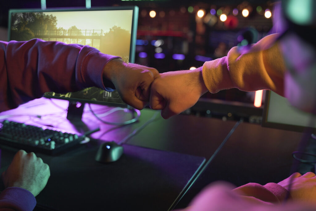 Two gamers fist bumping across gaming desks in a neon lit esports environment, symbolizing teamwork, partnership, and collaboration in the gaming industry.
