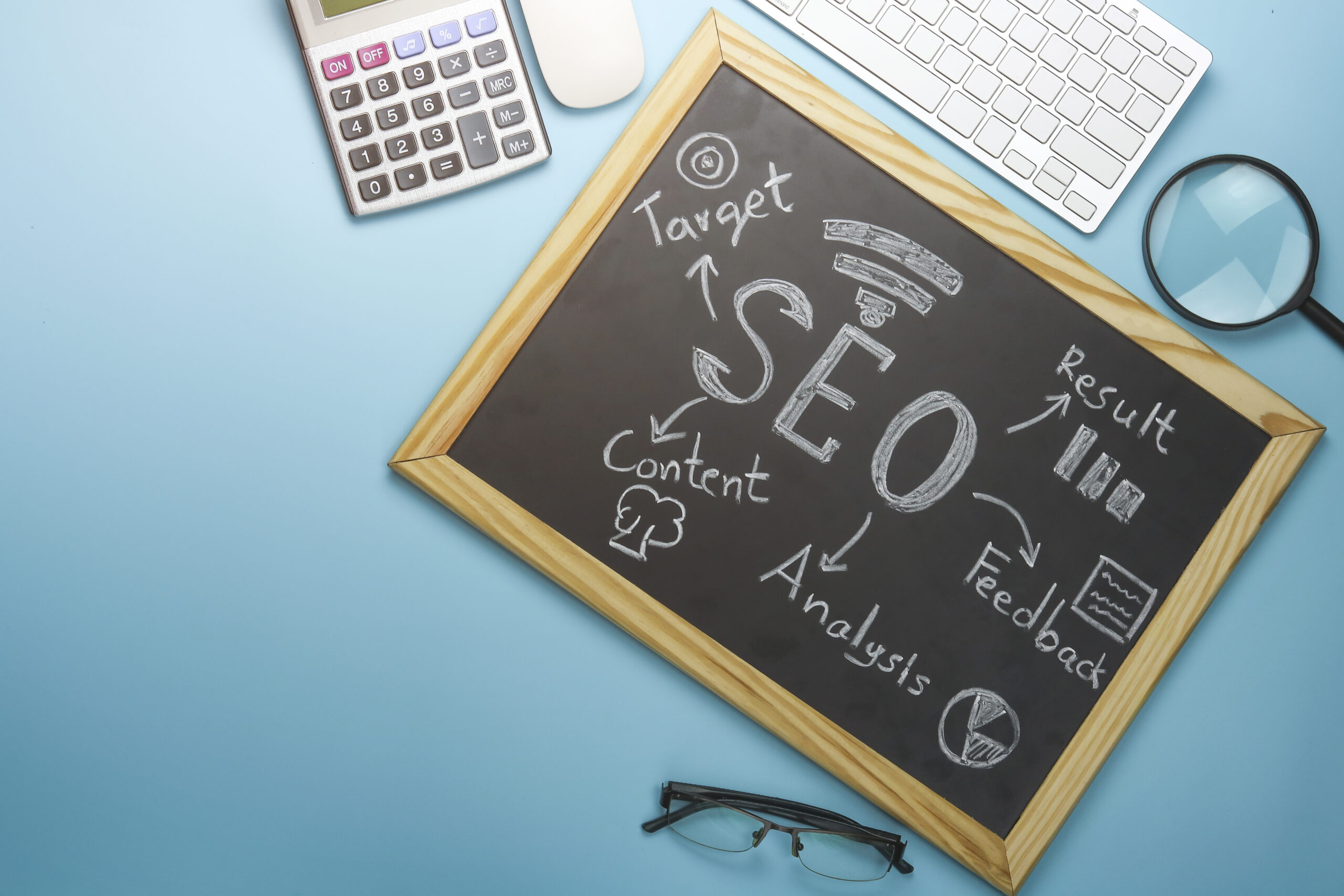 SEO strategy concept shown on a chalkboard with keywords like target, content, analysis, and results surrounded by office tools