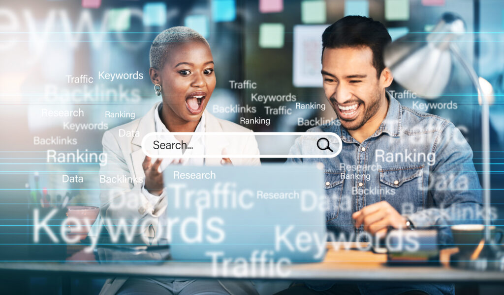 Two professionals smiling while looking at a laptop with an on-screen search bar and SEO-related keywords like traffic, rankings, and backlinks, representing keyword research and SEO success.