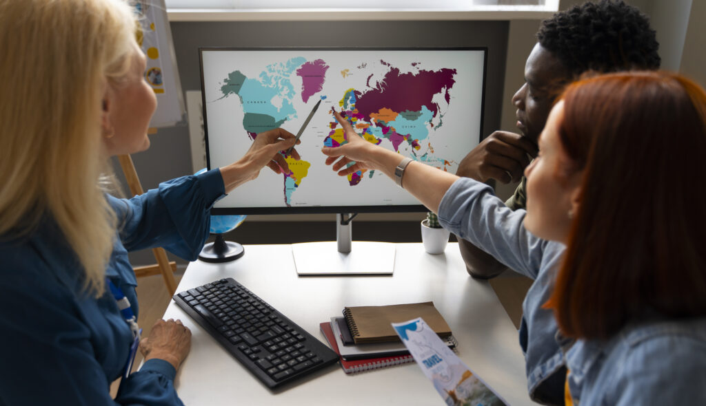Team reviewing a world map on a computer screen, discussing global market entry strategy and international expansion planning.