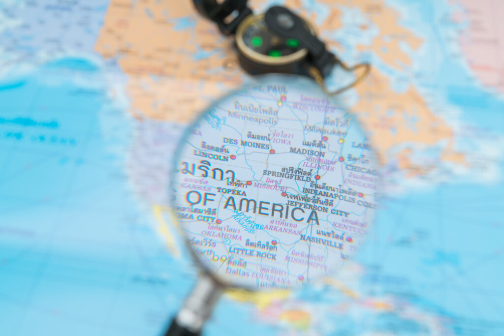 Magnifying glass highlighting the United States on a world map, representing North American market research and entry analysis.