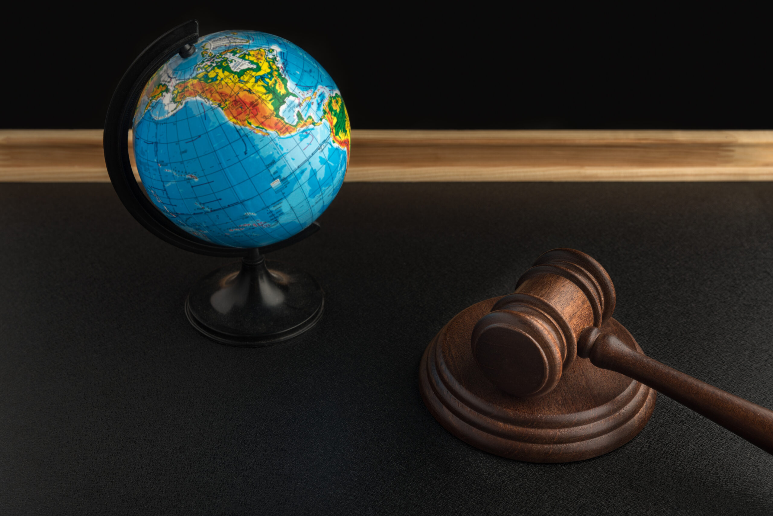 A judge’s gavel resting on a dark surface beside a small globe, symbolizing the intersection of law, global perspective, and legal decision making.