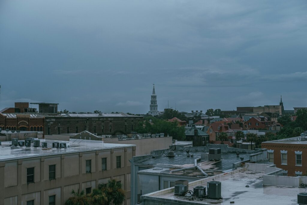 Rooftop view of a historic downtown cityscape under overcast skies, with a white church steeple rising above surrounding brick buildings and green trees.