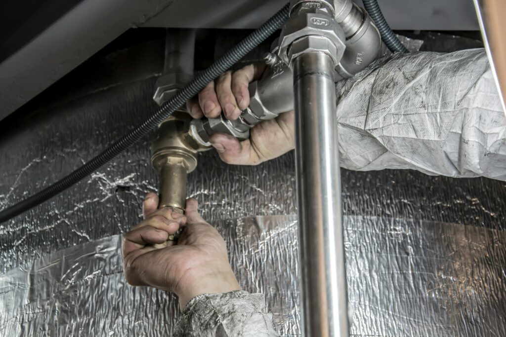 Close-up of a technician tightening industrial metal piping and valves while working on insulated mechanical equipment.