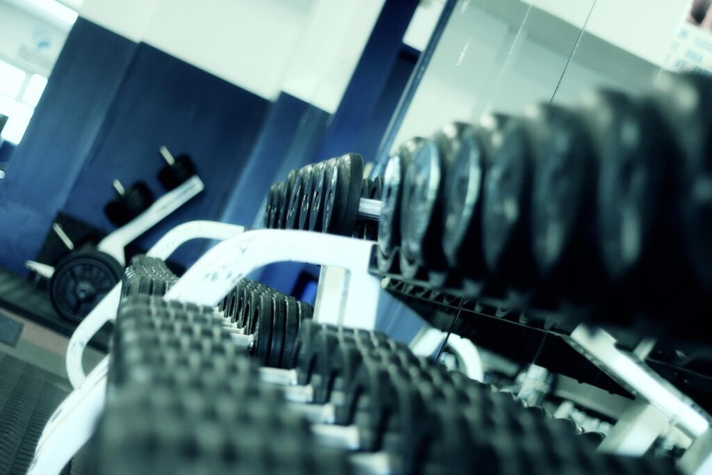 Close-up view of dumbbells lined up on a rack inside a modern gym with mirrored walls and fitness equipment in the background.