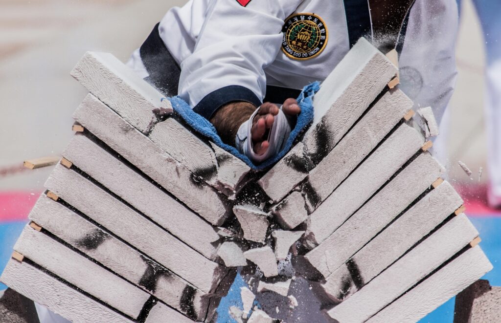 Martial artist in a taekwondo uniform performing a powerful hand strike to break stacked concrete blocks during a demonstration.