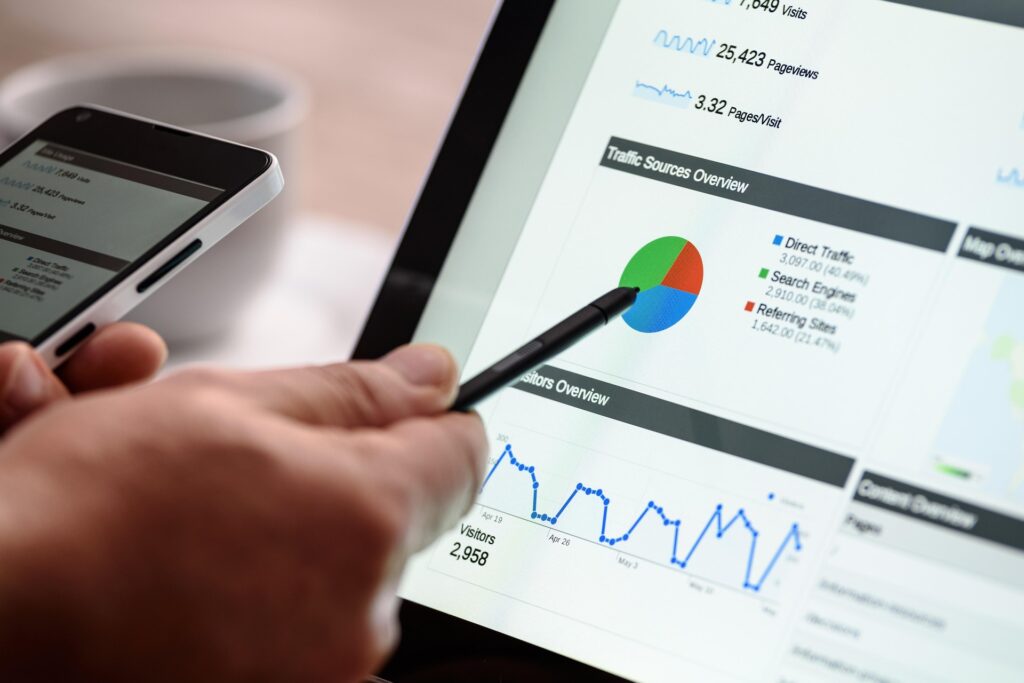 Person using a smartphone and stylus to review website traffic and analytics data on a tablet screen.
