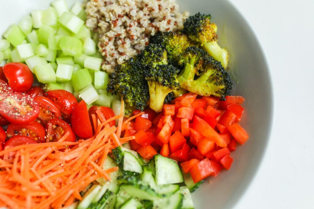 Vegetable bowl with quinoa, roasted broccoli, cucumber, tomatoes, carrots, and red bell peppers.