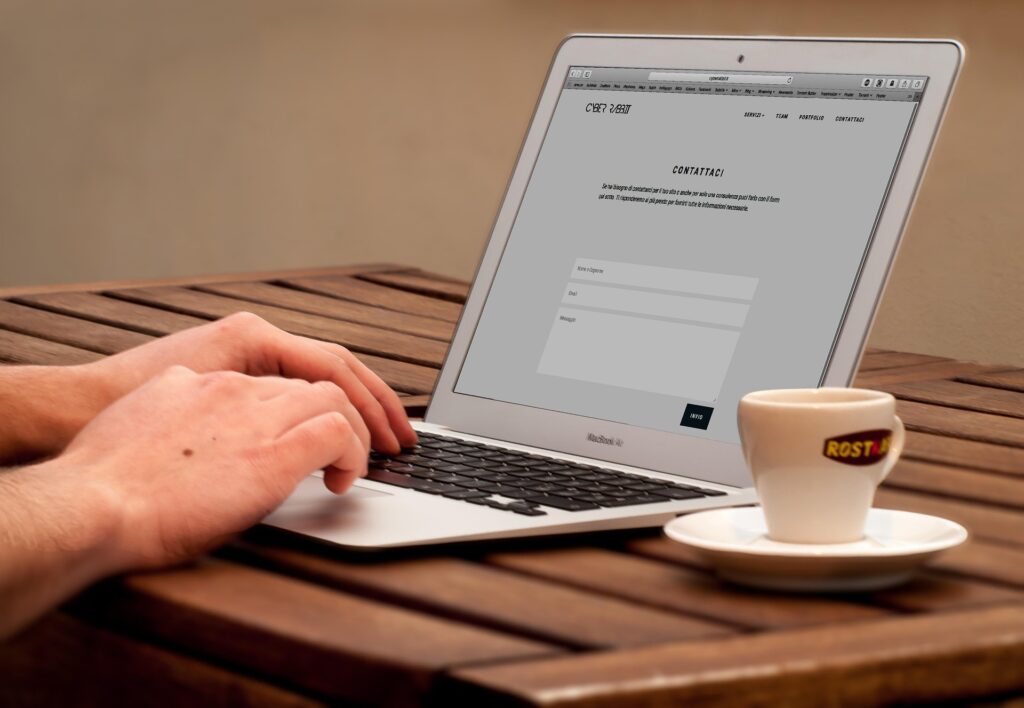 Person typing on a laptop displaying a contact form beside a cup of coffee.