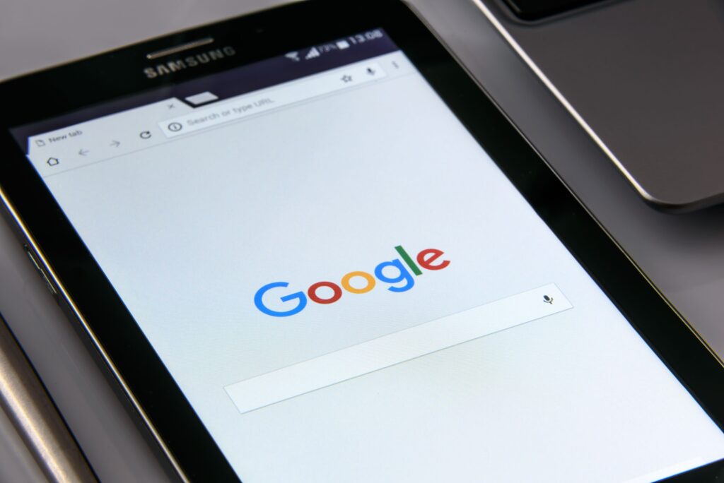 Samsung smartphone displaying the Google search homepage next to a laptop.