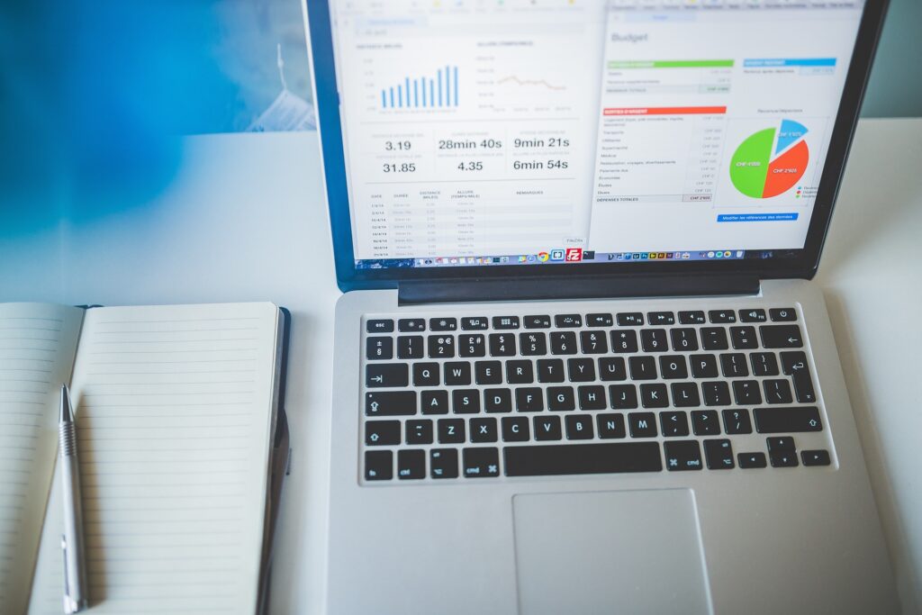 Laptop displaying charts and budget data beside an open notebook and pen on a desk.