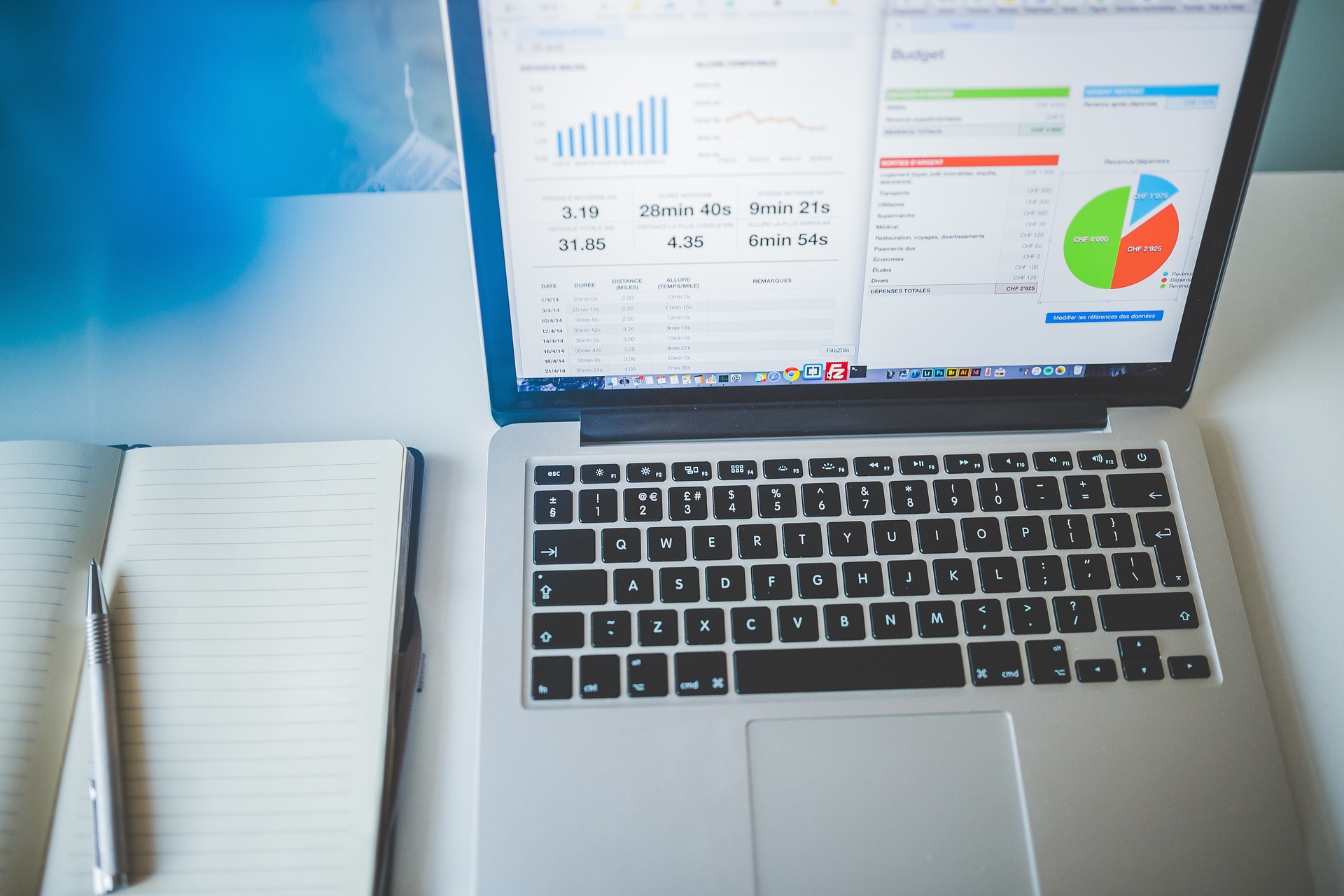 Laptop displaying charts and budget data beside an open notebook and pen on a desk.