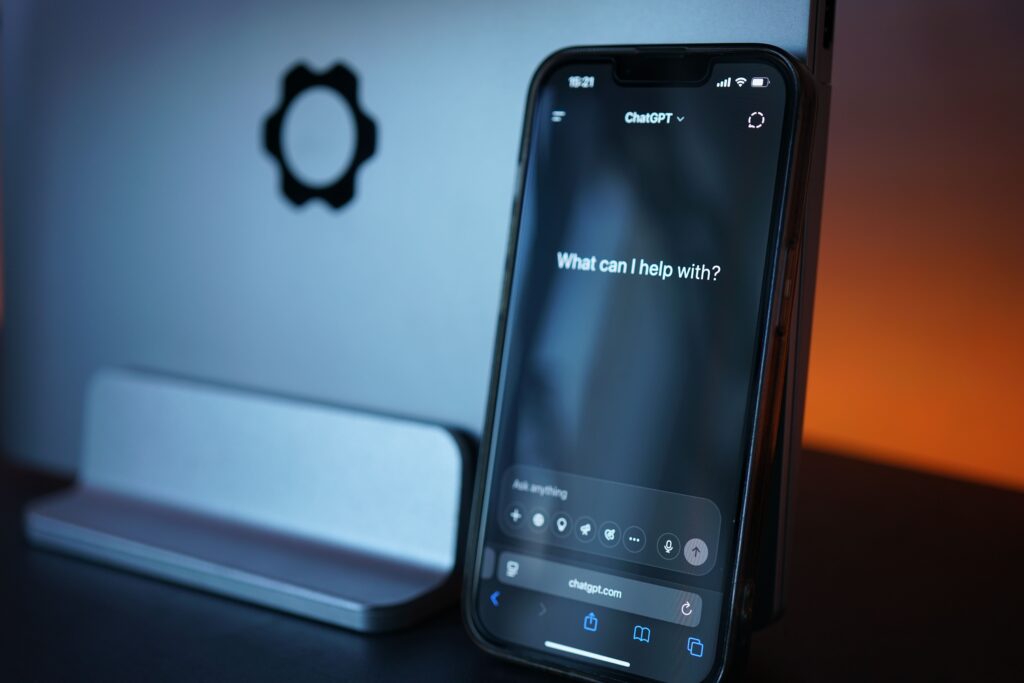 Smartphone displaying ChatGPT beside a laptop in blue and orange lighting.