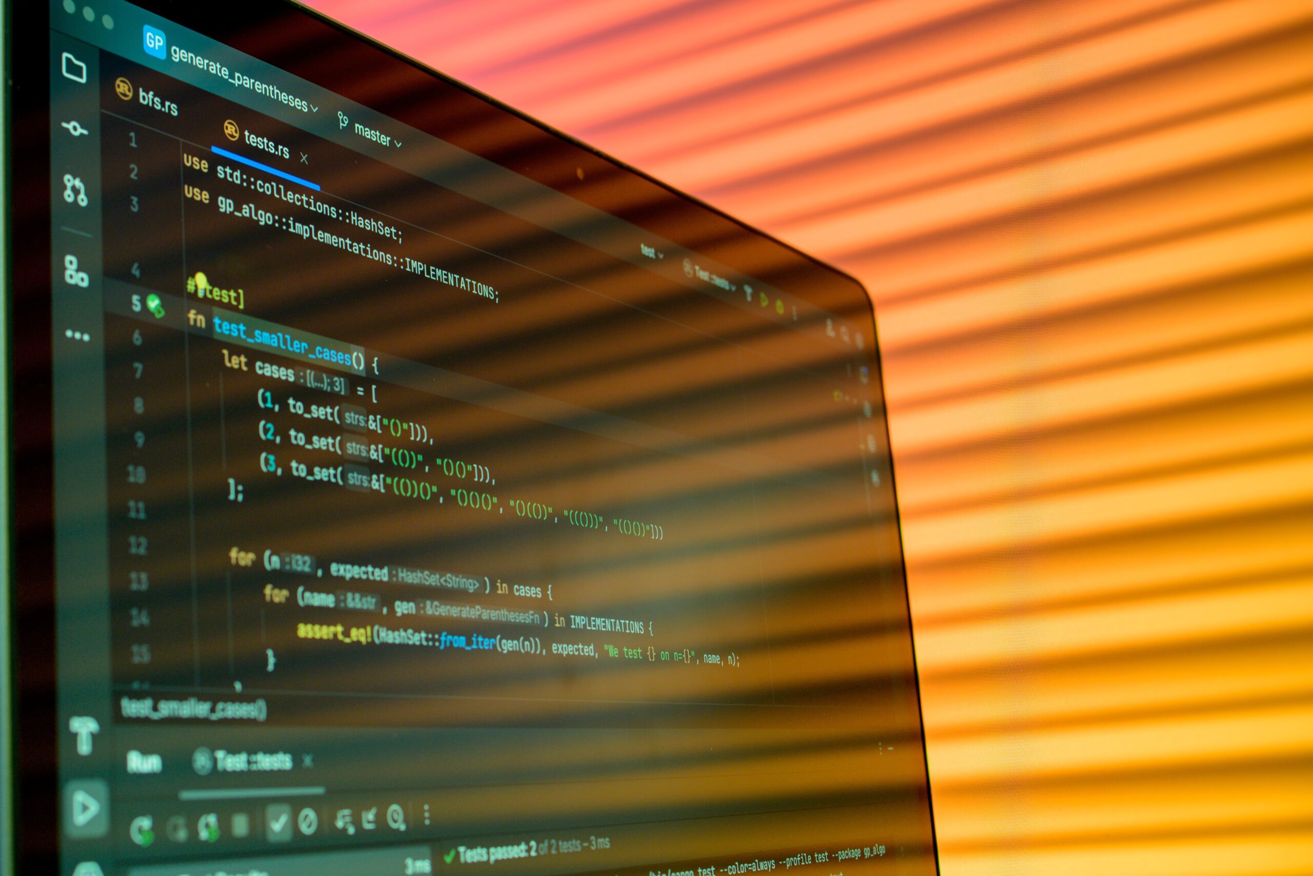 Computer monitor displaying programming code in a dark-themed editor against an orange-lit background.