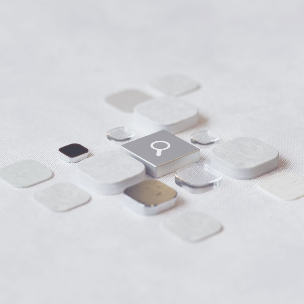 Abstract arrangement of metallic and white tiles surrounding a central search icon.