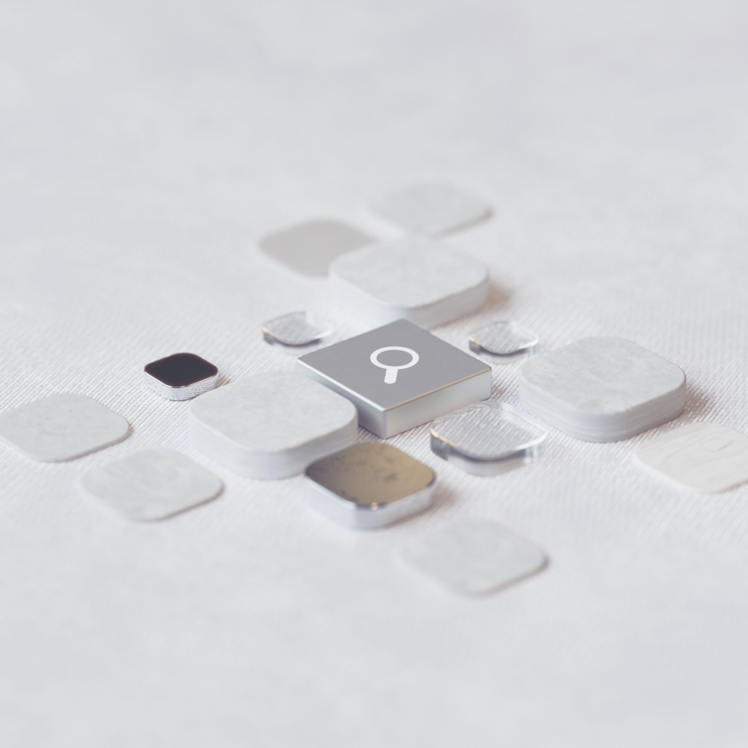 Abstract arrangement of metallic and white tiles surrounding a central search icon.