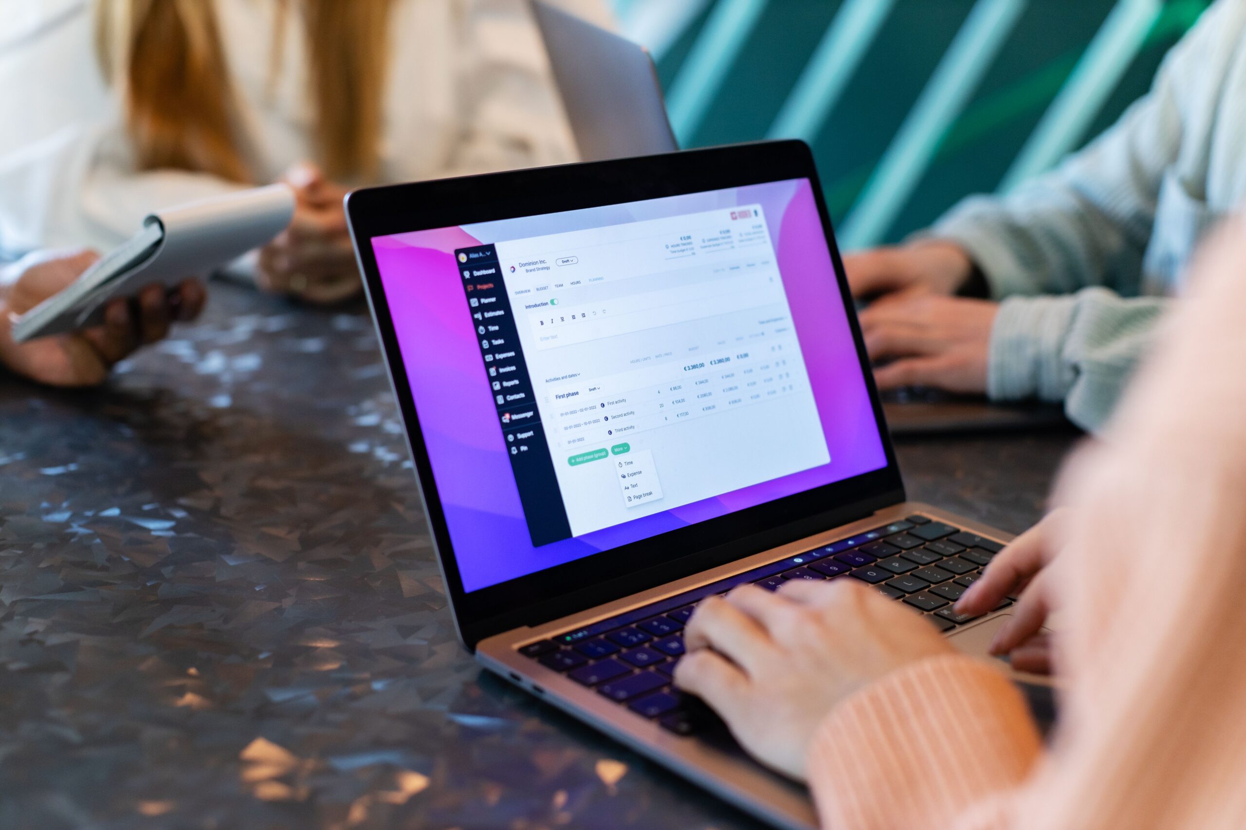 Team collaborating around a laptop displaying project management and financial data.