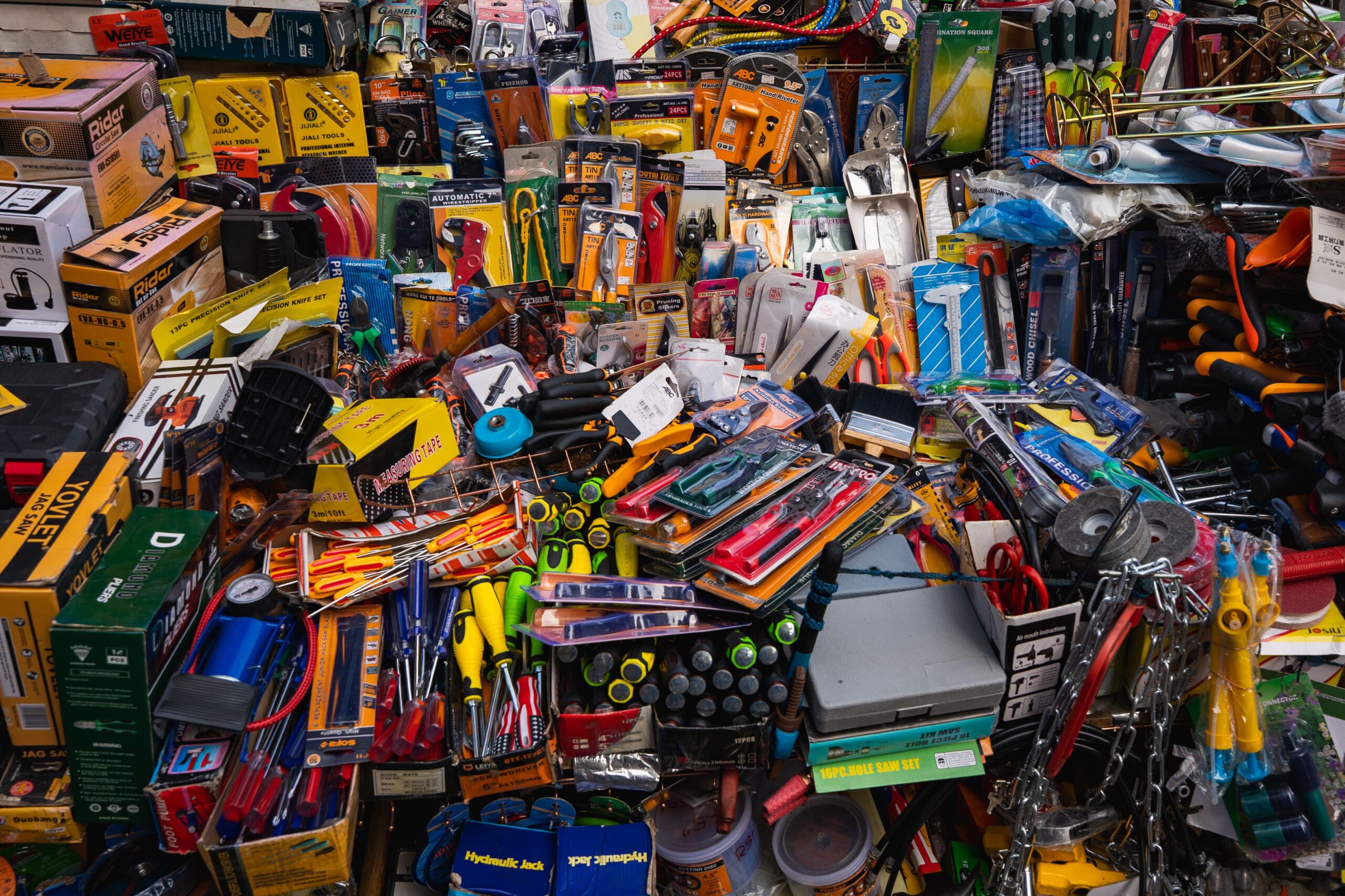 Crowded hardware market display filled with packaged hand tools, saws, screwdrivers, pliers, and measuring equipment.