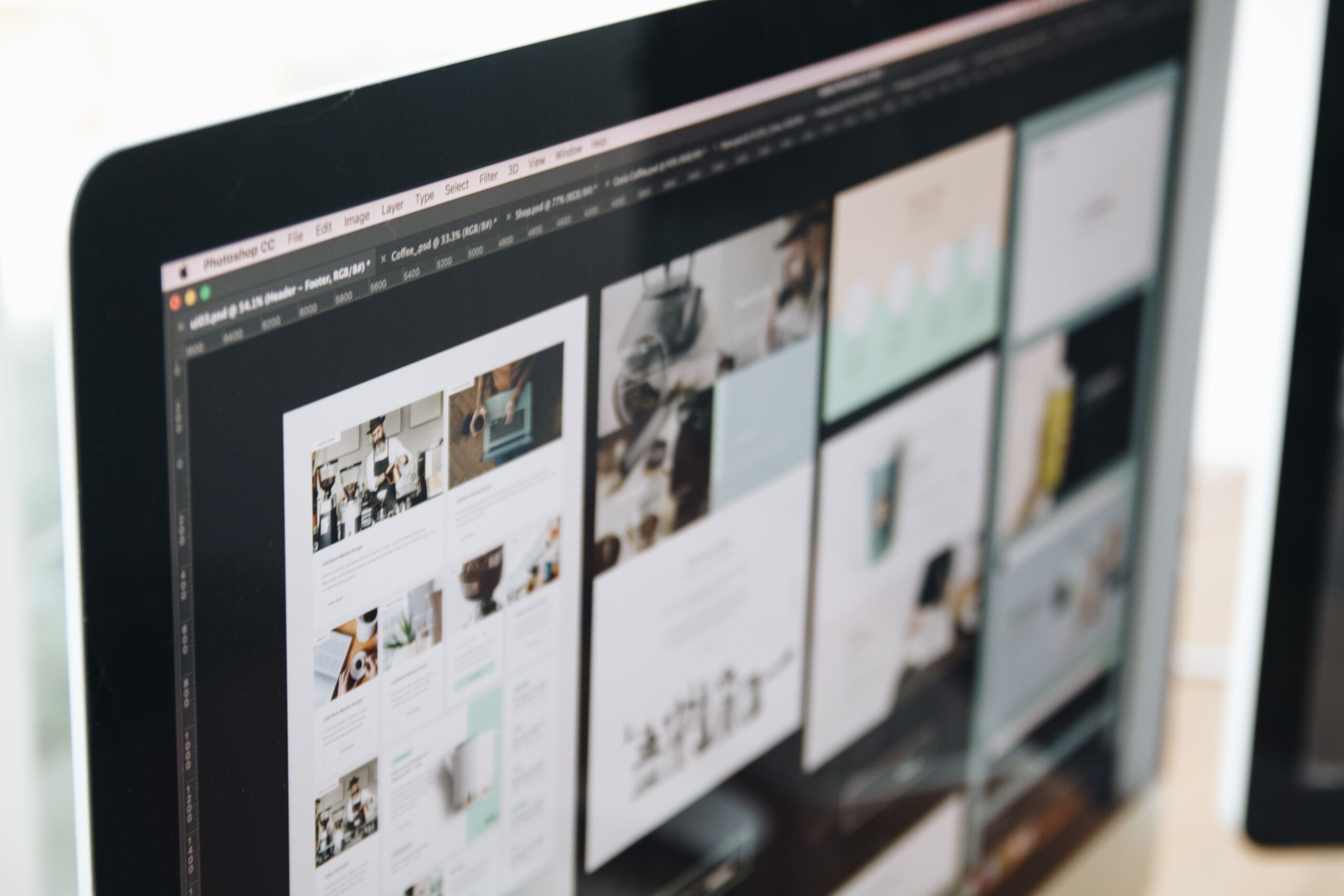 Computer monitor displaying website design layouts in Adobe Photoshop.