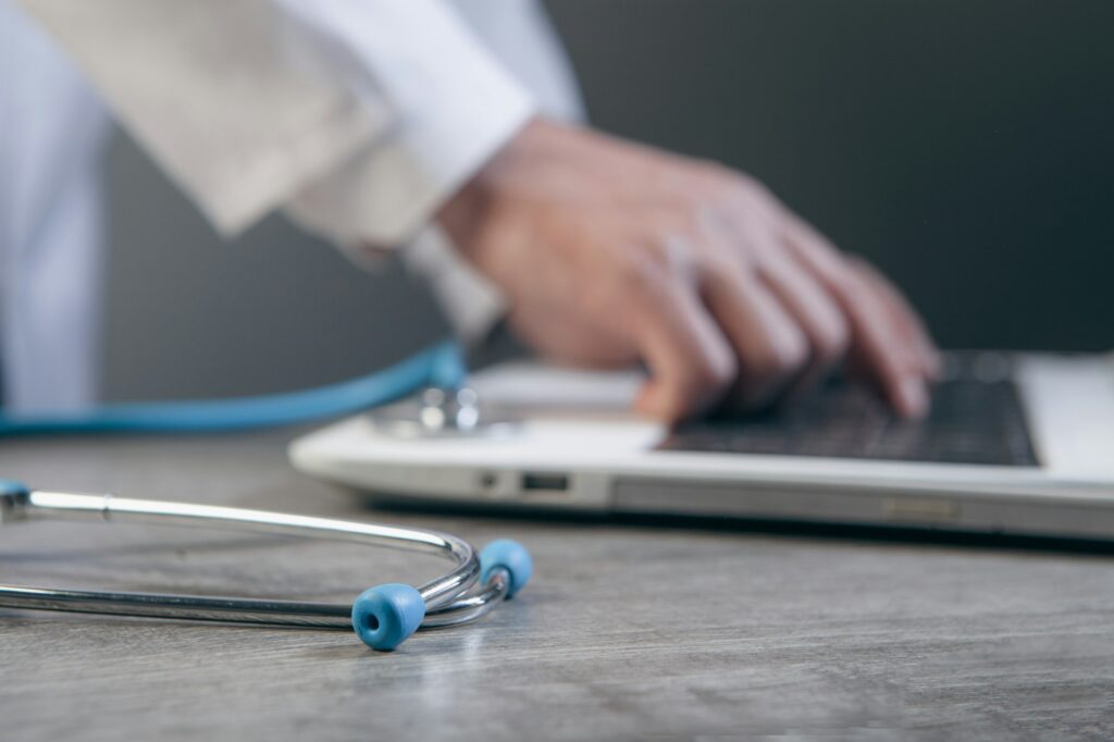 Doctor typing on a laptop with a stethoscope nearby
